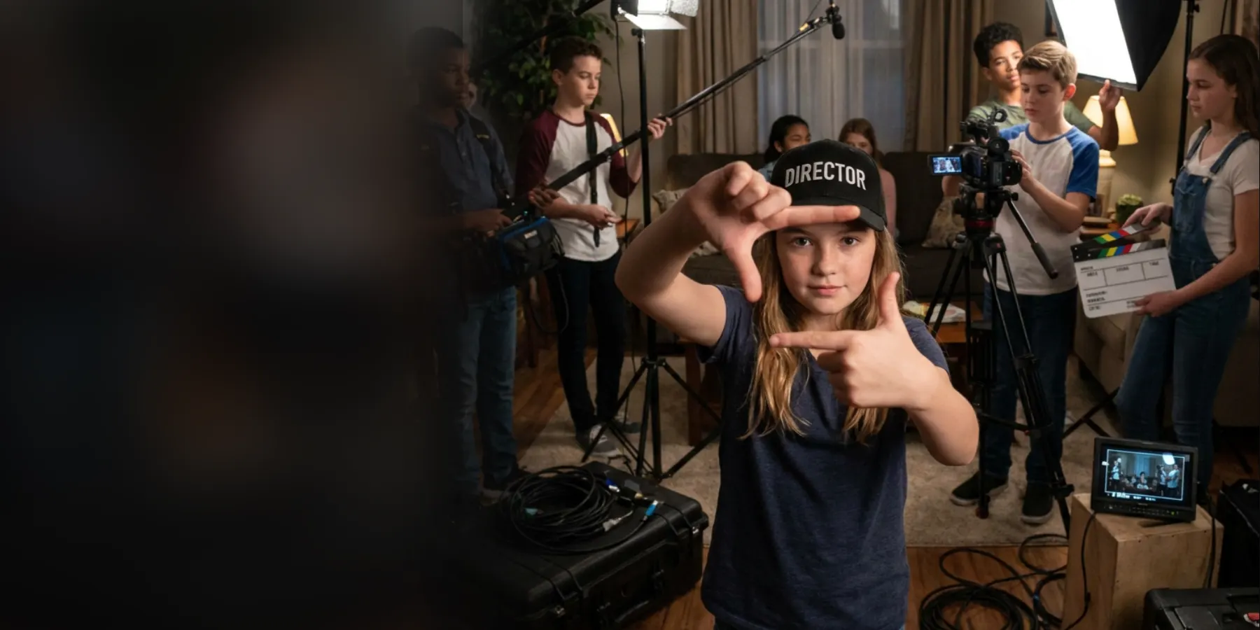A young camper in a DIRECTOR cap framing a shot with her hands while her crew runs lights, boom and camera behind her