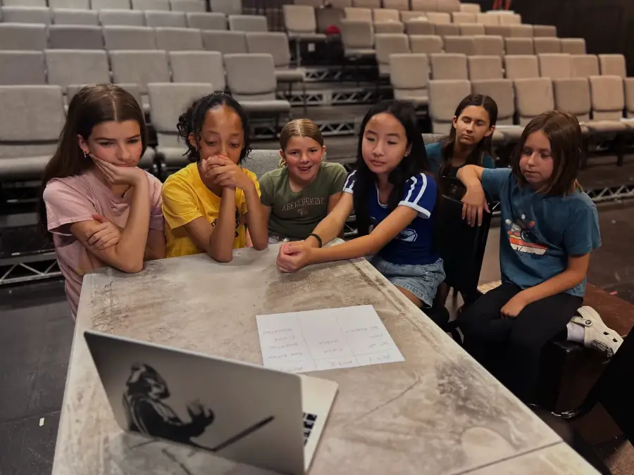 Six campers crowded round a laptop working out their three-act structure