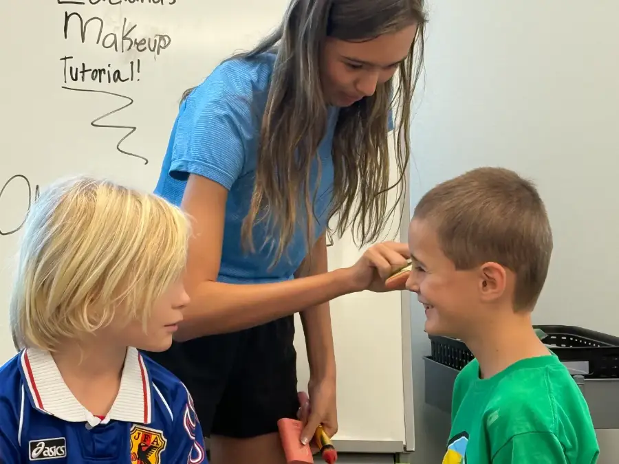 An instructor doing camp make-up on a young actor before his scene