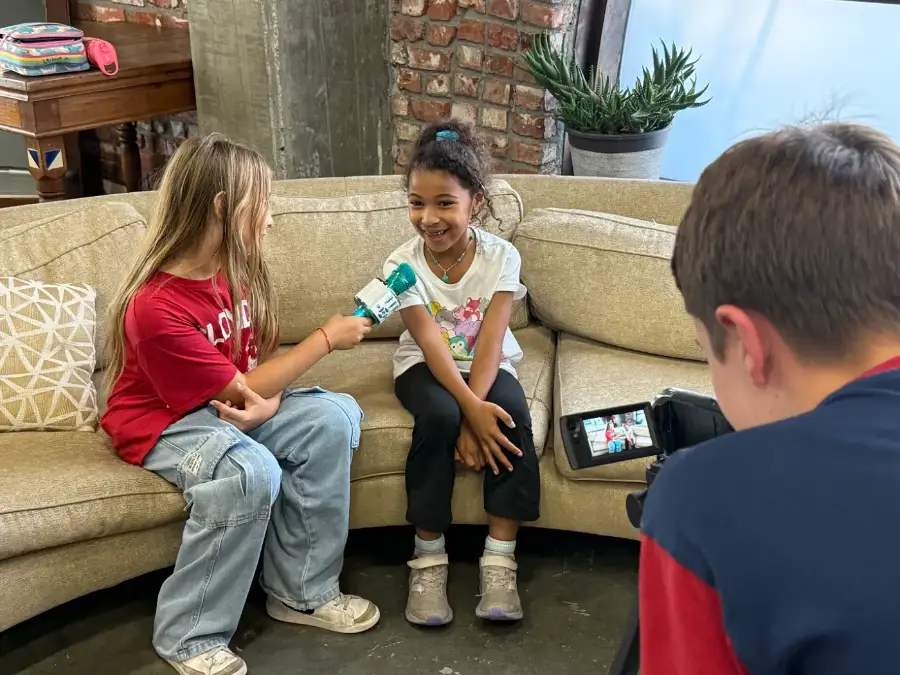 A camper interviewing her co-star on the sofa while another films
